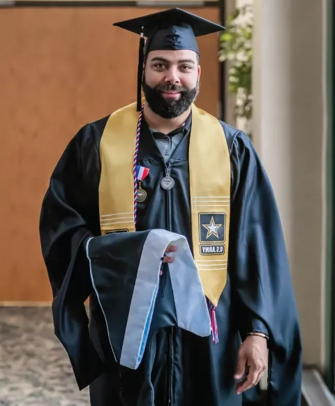 U.S. Army veteran wearing commencement gown and cap at graduation ceremony.