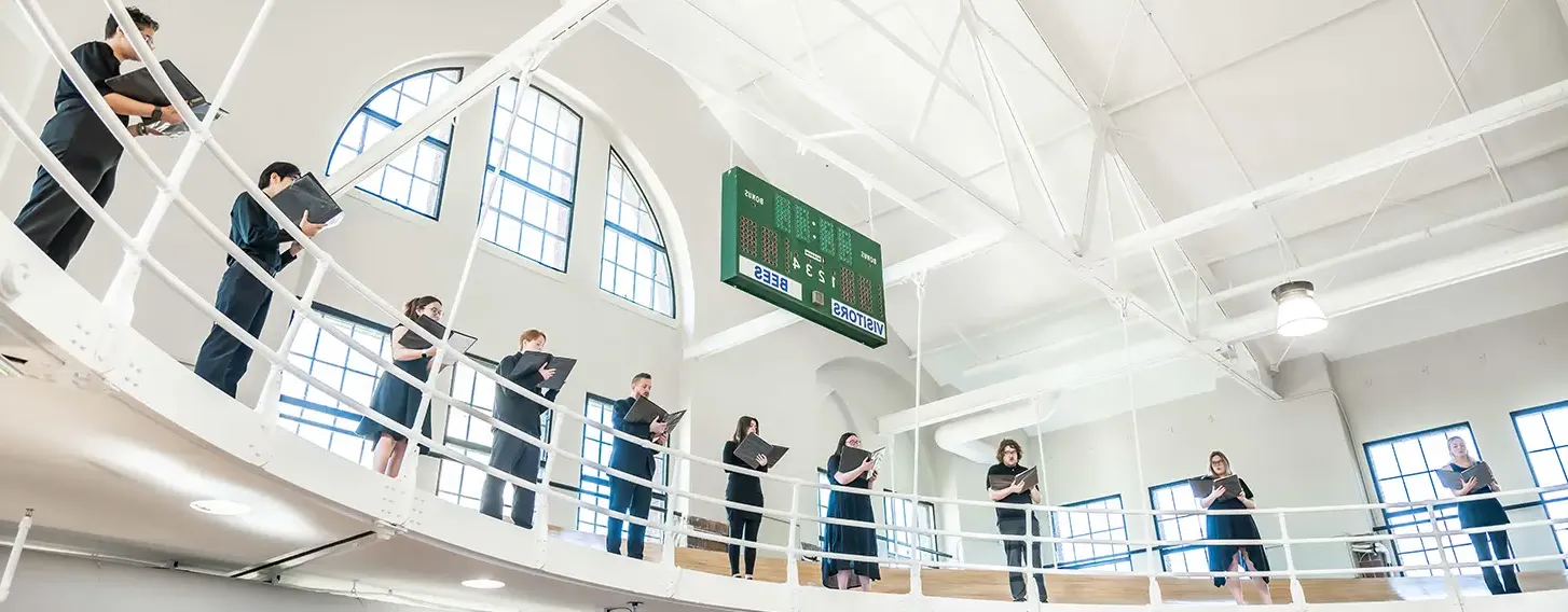 Several students standing around the Higgins balcony performing a song.